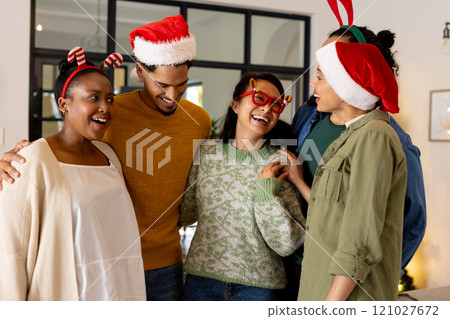 Wearing festive hats, multiracial friends laughing together at home during Christmas celebration 121027672