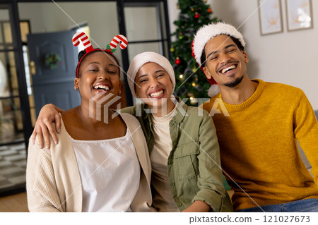 Young multiracial friends wearing festive hats smiling together by Christmas tree at home 121027673