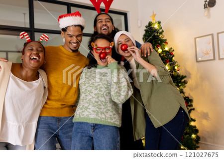 Young multiracial friends celebrating Christmas at home, wearing festive hats and laughing Young multiracial friends celebrating Christmas at home, wearing festive hats and laughing 121027675