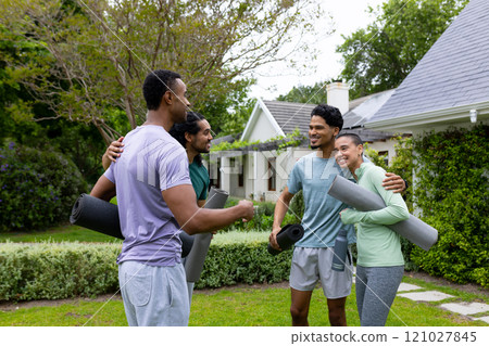 Young multiracial friends gathering outdoors with yoga mats, enjoying cheerful conversation 121027845