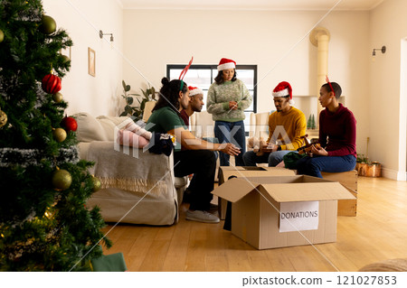 Young multiracial friends in Santa hats organizing holiday donations at home together 121027853