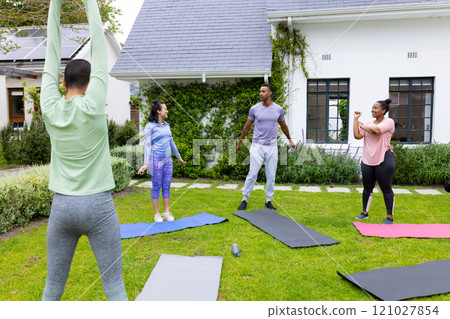 multiracial friends exercising together outdoors on yoga mats, enjoying group fitness session 121027854