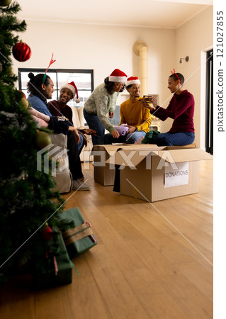 Young multiracial friends wearing Santa hats packing donation boxes at home during Christmas 121027855