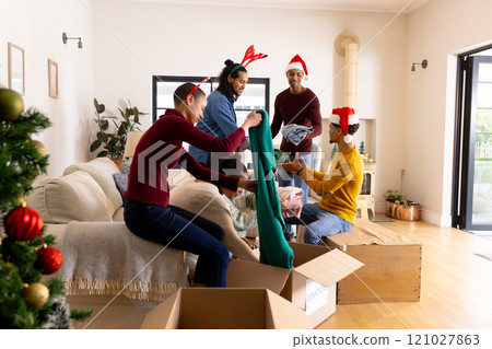 Christmas time, wearing festive hats, multiracial friends packing gifts in living room, at home Christmas time, wearing festive hats, multiracial friends packing gifts in living room, at home 121027863