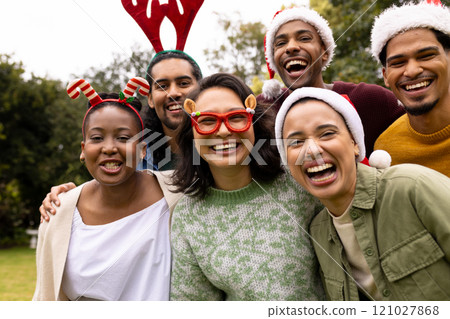 Wearing festive hats, multiracial friends celebrating Christmas outdoors, laughing together joyfully Wearing festive hats, multiracial friends celebrating Christmas outdoors, laughing together joyfully 121027868