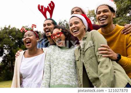 Wearing festive hats, multiracial friends laughing together outdoors during Christmas celebration Wearing festive hats, multiracial friends laughing together outdoors during Christmas celebration 121027870