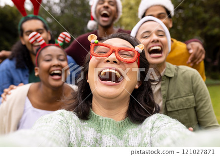 Christmas time, taking a selfie, laughing together outdoors, multiracial friends in park Christmas time, taking a selfie, laughing together outdoors, multiracial friends in park 121027871