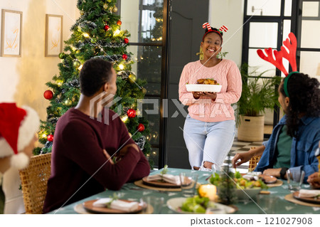 Multiracial friends celebrating christmas dinner together, woman serving roast chicken, at home Multiracial friends celebrating christmas dinner together, woman serving roast chicken, at home 121027908