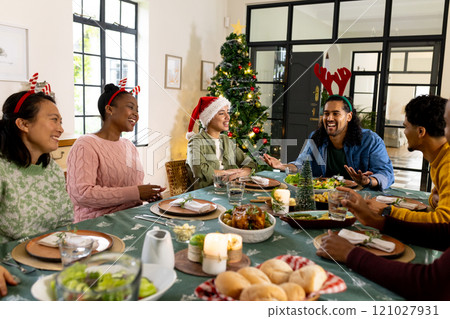 Celebrating Christmas at home, multiracial friends laughing and sharing festive dinner together Celebrating Christmas at home, multiracial friends laughing and sharing festive dinner together 121027931