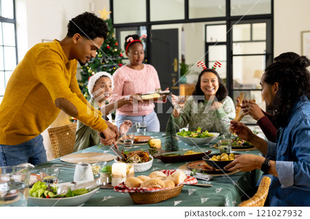 Sharing laughter, multiracial friends celebrating christmas dinner together, at home Sharing laughter, multiracial friends celebrating christmas dinner together, at home 121027932