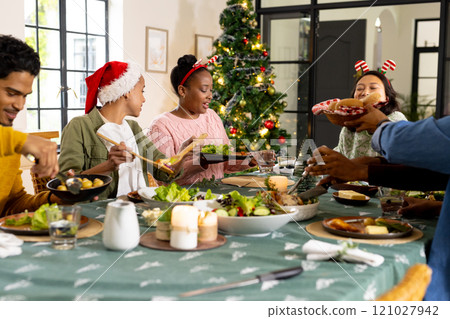 Young multiracial friends enjoying festive christmas dinner together, at home 121027942