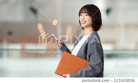 Smiling woman/businesswoman holding a smartphone and a binder Smiling woman/businesswoman holding a smartphone and a binder 121028056