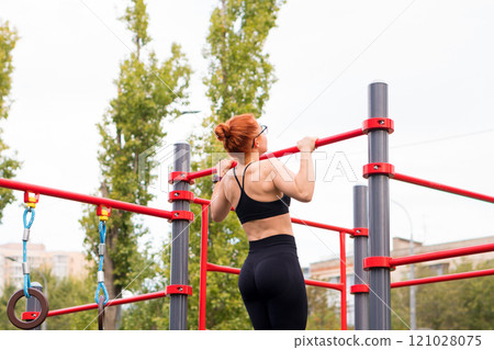 Woman lifting herself on red pull-up bar 121028075