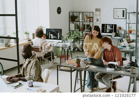 High angle shot of cozy office full of digital devices and furniture, biracial workers interacting with each other and working High angle shot of cozy office full of digital devices and furniture, biracial workers interacting with each other and working 121028177