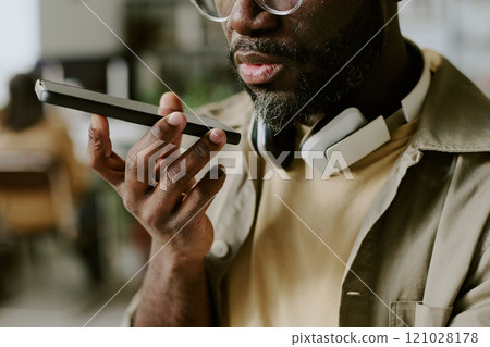 Medium close up of unrecognizable African American man with headphones around neck recording voice message 121028178