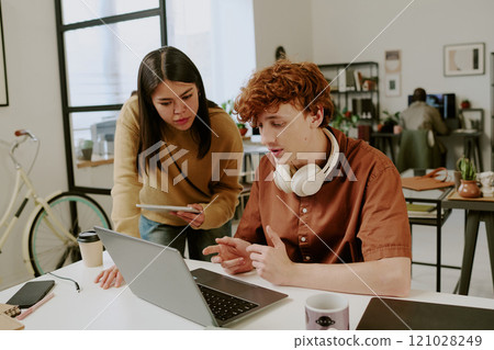 Medium close up of Caucasian male and female coworkers discussing work together in modern office, they looking at monitor Medium close up of Caucasian male and female coworkers discussing work together in modern office, they looking at monitor 121028249
