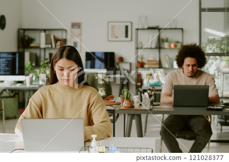 Biracial coworkers sitting at work desks and programming in modern office of IT company equipped with digital devices and extra workspaces 121028377