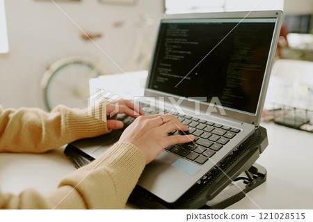 Medium close up of unrecognizable female hand with gold ring typing codes on laptop located on cooling pad Medium close up of unrecognizable female hand with gold ring typing codes on laptop located on cooling pad 121028515