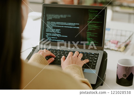 Back view of unrecognizable woman typing on laptops keyboard to write codes in cozy office Back view of unrecognizable woman typing on laptops keyboard to write codes in cozy office 121028538