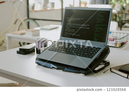 Medium close up of laptop with codes on cooling pad in empty office of IT company 121028568