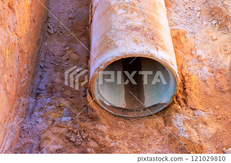 Exposed concrete pipe rests in dirt, surrounded by soil, gravel at construction site. Exposed concrete pipe rests in dirt, surrounded by soil, gravel at construction site. 121029810