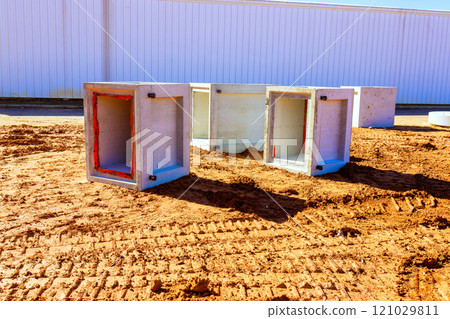Concrete drainage boxes are arranged on dirt surface at construction site, showcasing industrial materials. Concrete drainage boxes are arranged on dirt surface at construction site, showcasing industrial materials. 121029811