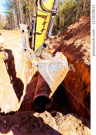 An excavator digs into earth to lay pipeline amidst to laying concrete pipe 121029812