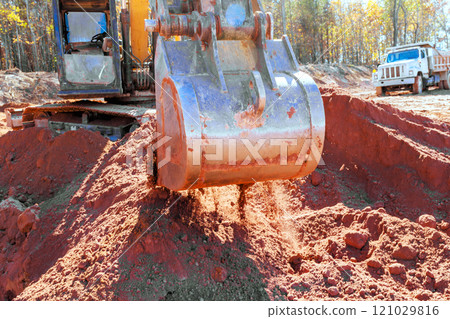 Construction equipment excavator excavated actively moving red soil at construction site during earth moving. Construction equipment excavator excavated actively moving red soil at construction site during earth moving. 121029816
