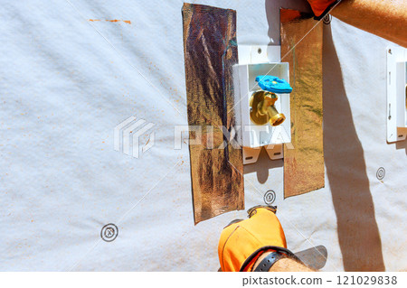 Worker installing wall installation material near wall water gold tape outside for home improvement project Worker installing wall installation material near wall water gold tape outside for home improvement project 121029838