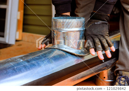 Contractor working with metal duct, securing components for HVAC heating ventilation system with construction site 121029842