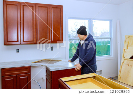 Contractor is carefully placing countertop in newly renovated kitchen with wooden cabinets during construction 121029865