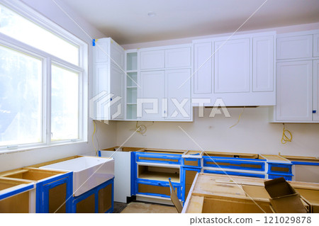 New kitchen construction underway featuring white cabinets house sink along with unfinished cabinetry blue masking tape for protection 121029878