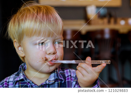 Young child with blond hair is savoring sugary treat, holding clear straw with chocolate stains on his lips warm interior adds to cozy ambiance. 121029883