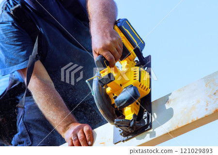 Skilled worker operates circular saw, cutting wood frame on under construction project at work area 121029893