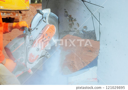 Worker uses concrete saw to cut drainage piece of pillar in build works area at construction location. 121029895