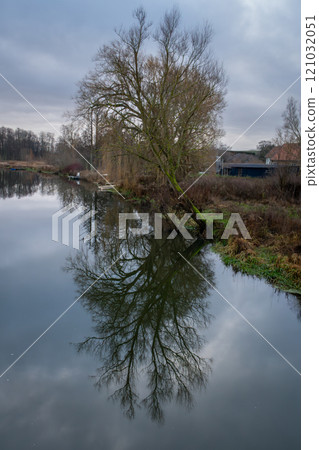 A tree gives a beautiful reflection in a river. A dark sky with clouds in the background 121032051