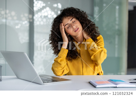 Businesswoman feeling stressed with headache at desk using laptop. Concept of stress, burnout, and work pressure in office setting and modern business environment. 121032324