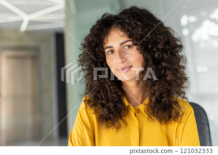 Latin American businesswoman with curly hair wearing yellow blouse. Expresses professionalism, confidence, approachability in modern office. Ideal for corporate, leadership, business themes. Latin American businesswoman with curly hair wearing yellow blouse. Expresses professionalism, confidence, approachability in modern office. Ideal for corporate, leadership, business themes. 121032333