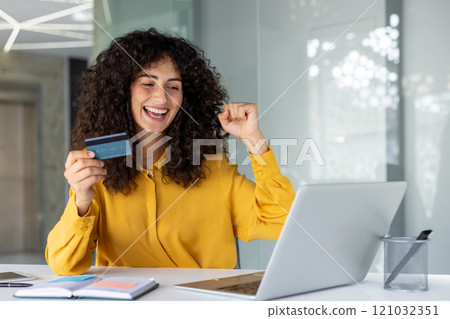 Happy woman in office celebrates successful online shopping with credit card and laptop. She shows excitement and success in financial transaction, symbolizing digital freedom and happiness. Happy woman in office celebrates successful online shopping with credit card and laptop. She shows excitement and success in financial transaction, symbolizing digital freedom and happiness. 121032351