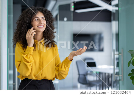 A young professional woman communicates using her smartphone in a modern office environment. Her cheerful expression suggests a positive and successful conversation A young professional woman communicates using her smartphone in a modern office environment. Her cheerful expression suggests a positive and successful conversation 121032464