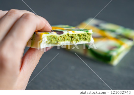 Piece of trend Dubai white chocolate with pistachio paste and kataifi dough in woman hand. Confectionery handmade sweets at home in the kitchen.  121032743