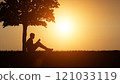 Man reading a book under a tree in nature at sunset. Silhouette of a person reading a book. 121033119