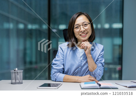 Asian woman businesswoman seated at her office desk, smiling confidently with a planner in front. Professional and approachable, she exemplifies modern corporate success and positivity. Asian woman businesswoman seated at her office desk, smiling confidently with a planner in front. Professional and approachable, she exemplifies modern corporate success and positivity. 121033518