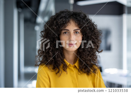 Confident woman standing in modern office. Wearing yellow blouse and expressing warmth and approachability. Background of contemporary workspace enhances professional vibe. Confident woman standing in modern office. Wearing yellow blouse and expressing warmth and approachability. Background of contemporary workspace enhances professional vibe. 121033538