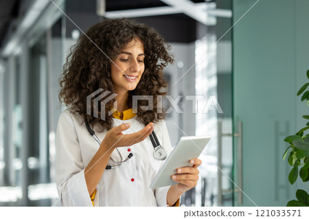 Healthcare professional with curly hair using tablet for video call in modern office. Focused on digital communication, remote consultation, technology, healthcare innovation. 121033571