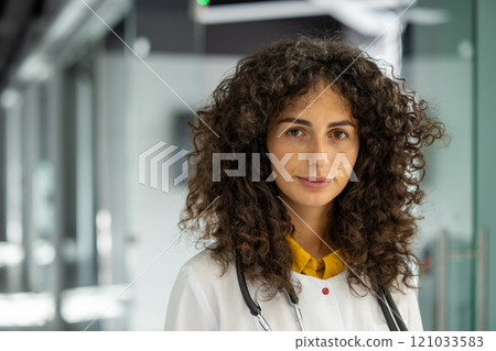 Professional female doctor with curly hair in hospital setting, wearing stethoscope. Represents healthcare, confidence, and medical service. Ideal image for medical and professional themes. Professional female doctor with curly hair in hospital setting, wearing stethoscope. Represents healthcare, confidence, and medical service. Ideal image for medical and professional themes. 121033583