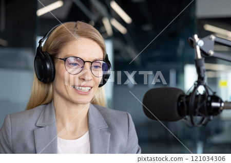 A mature businesswoman engages in a professional podcast, wearing headphones and speaking into a microphone. Her poised demeanor and focus reflect expertise and confidence. A mature businesswoman engages in a professional podcast, wearing headphones and speaking into a microphone. Her poised demeanor and focus reflect expertise and confidence. 121034306
