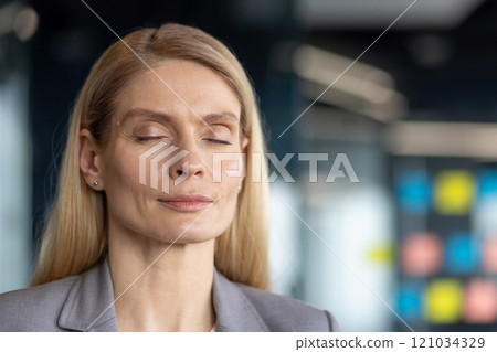 Mature woman businesswoman with closed eyes in office setting, embracing calmness, focus, mindfulness. Portrays serenity, meditation, tranquility at workplace. Mature woman businesswoman with closed eyes in office setting, embracing calmness, focus, mindfulness. Portrays serenity, meditation, tranquility at workplace. 121034329