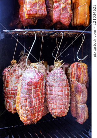 Smoker filled with variety of meat cuts bacon hanging from hooks combine to make delicious culinary tradition in smokehouse 121034623
