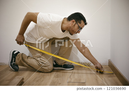 Adult man with a tape measure installing a parquet laminate floor in a business 121036690